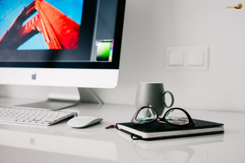 Foto de um computador em uma mesa brancos, com caderno, óculos e xícara ao lado. Imagem ilustrativa para texto franquias baratas para trabalhar em casa.