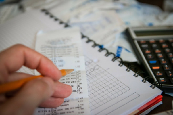 Imagem de uma mão fazendo anotações em uma conta e uma calculadora ao lado.