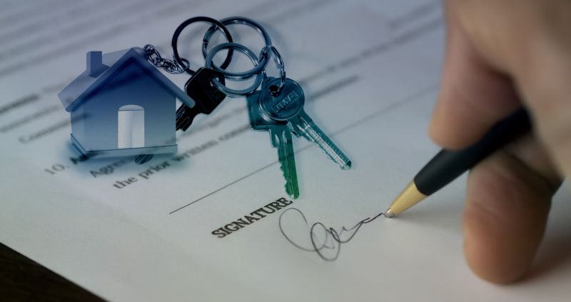 Foto da mão de uma pessoa assinando um contrato com uma chave de casa ao lado. Imagem ilustrativa para texto franquia de seguro.