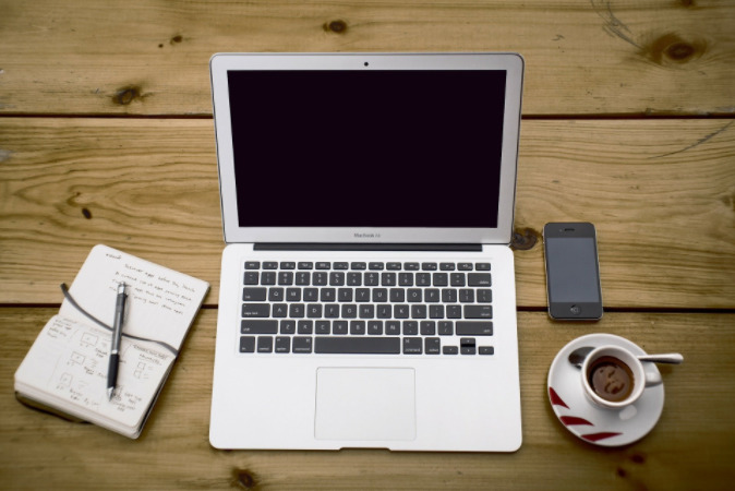 Foto de uma mesa de madeira com computador, caderno e xícara de café ao lado. Imagem ilustrativa para texto franquia virtual.