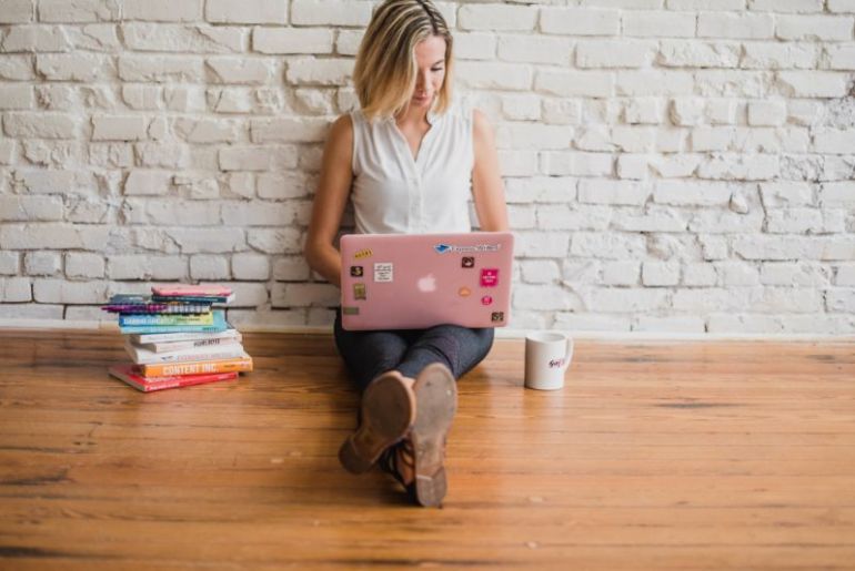 Foto de uma mulher sentada no chão com computador, livros e uma caneca. Imagem ilustrativa para texto melhor negócio para investir.