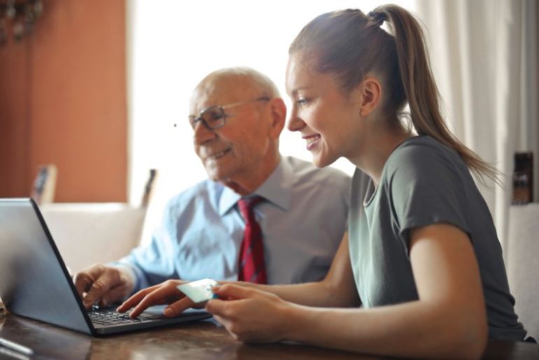 Mulher jovem ajudando idoso com pagamento pela internet usando notebook