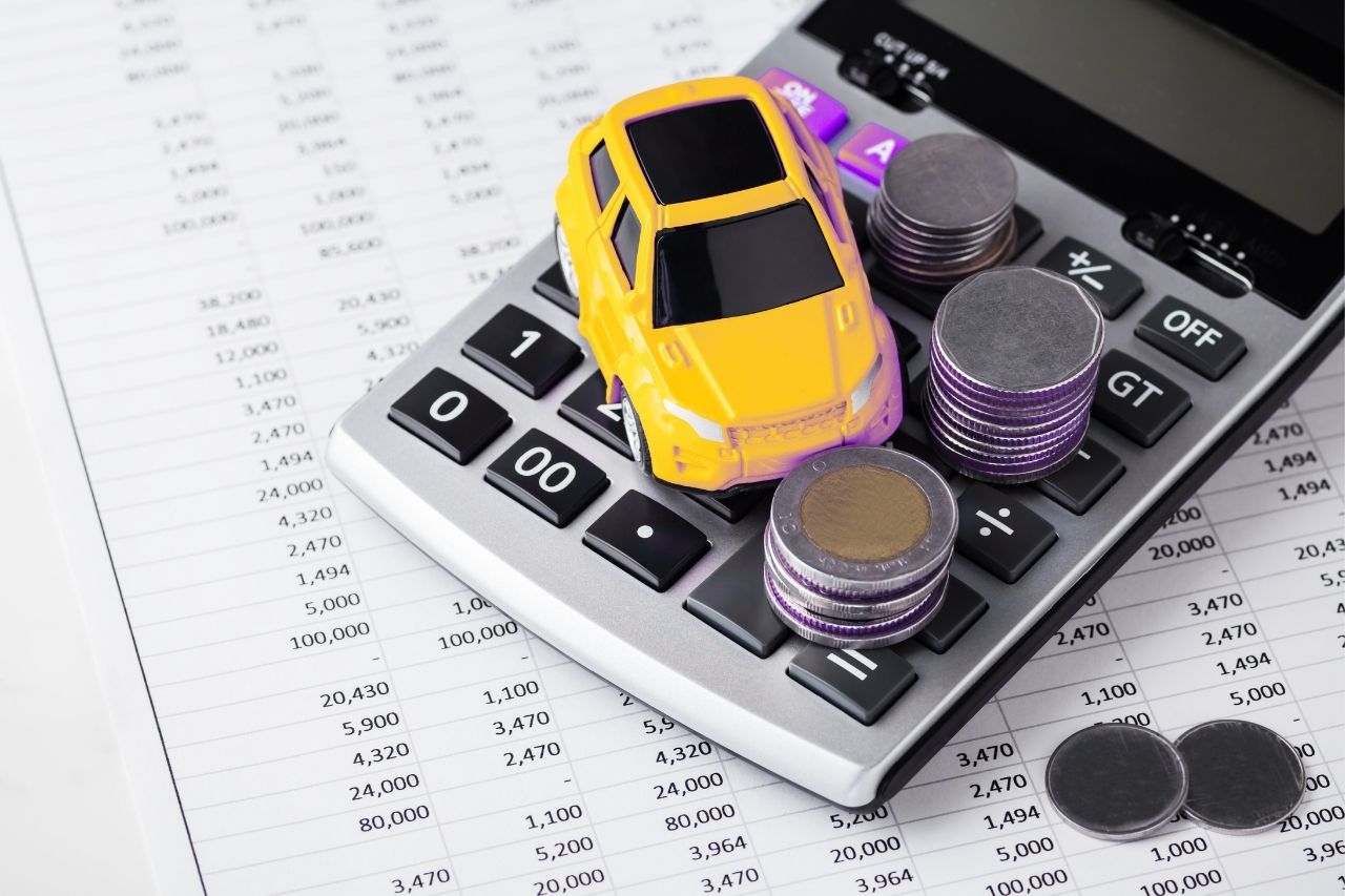 Calculadora com carro em miniatura e moedas, representando o custo do empréstimo para motorista de aplicativo e a análise do crédito