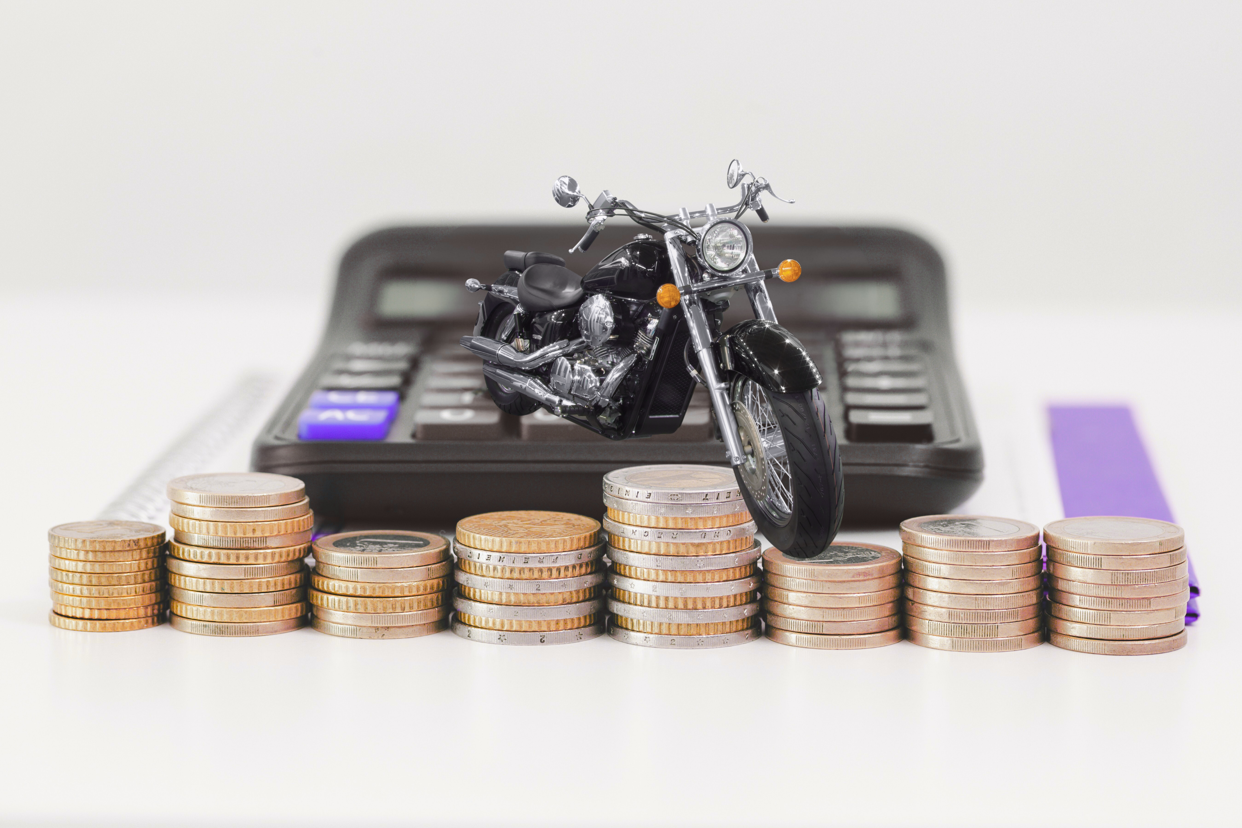 Moto posicionada sobre pilhas de moedas, com calculadora ao fundo, representando o cálculo de valor, juros e custos no empréstimo com garantia de moto